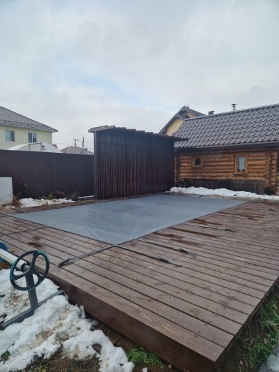 Композитный бассейн с защитным тентом на террасе из темного дерева около деревянного сруба